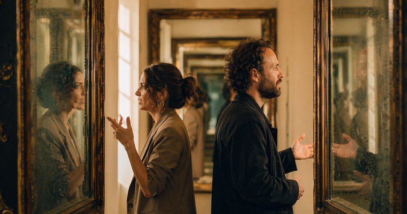 Dos personas espalda contra espalda en galería entre dos espejos enfrentados creando reflejo infinito